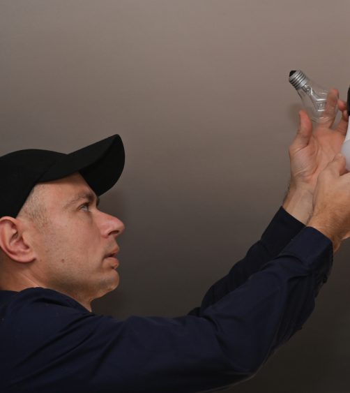 the electrician unscrewed the incandescent lamp and replaced it with an LED lamp. the concept of energy economy The man unscrewed the incandescent bulb and replaced it with an LED lamp